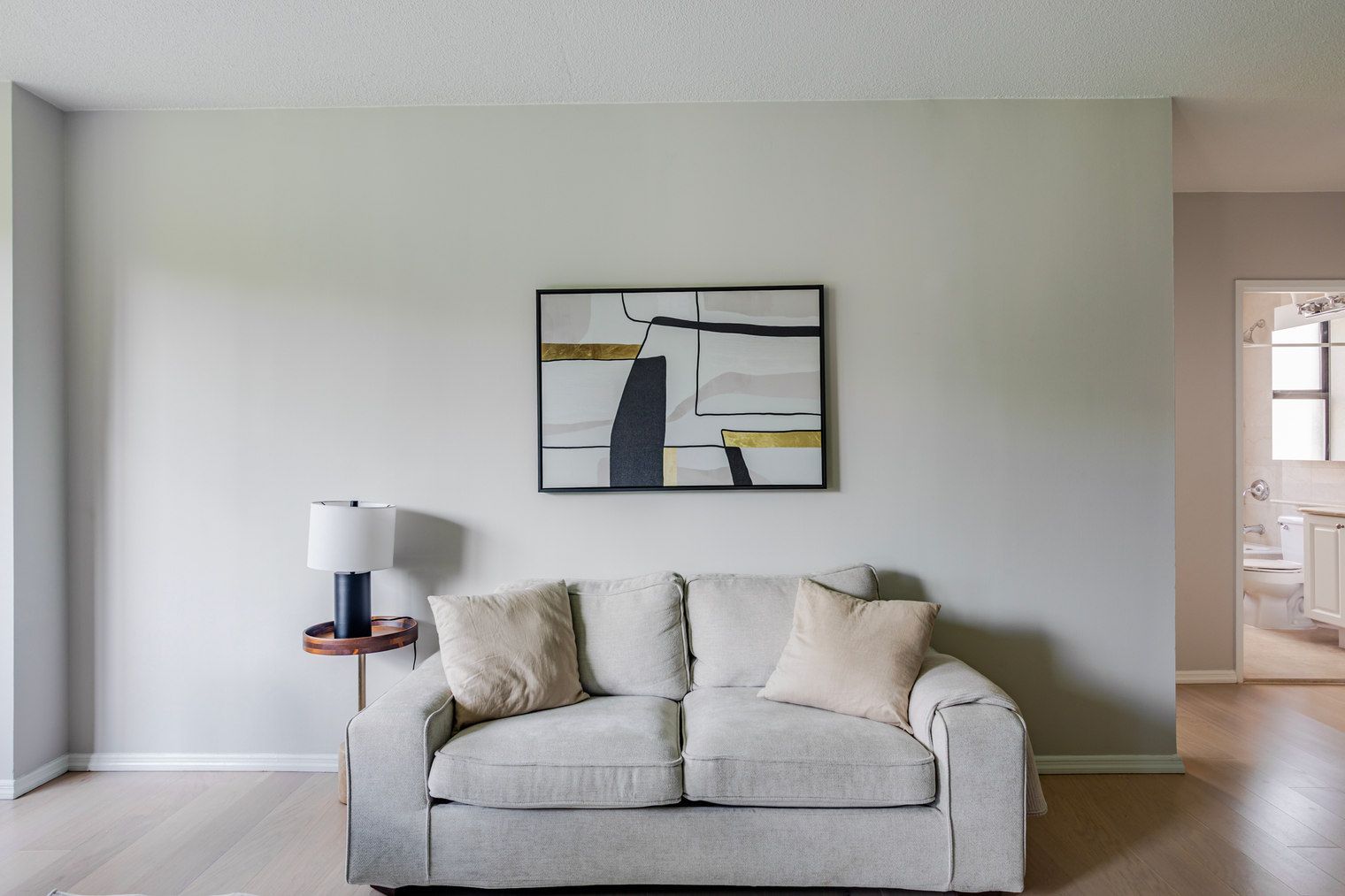 A living room with a grey sofa, a side table with a lamp, and a framed abstract painting on the wall.