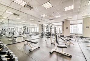 Ein großzügiger Fitnessraum mit unterschiedlichen Trainingsgeräten, großen Fenstern und einer Spiegelwand.