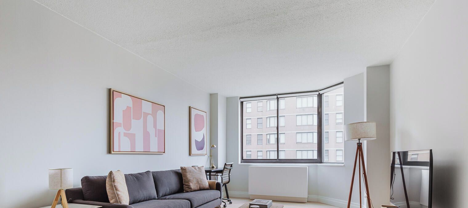 Ein modernes Wohnzimmer mit großem Fenster, einer Couch, einer Lampe und gerahmten Kunstwerken an der Wand.