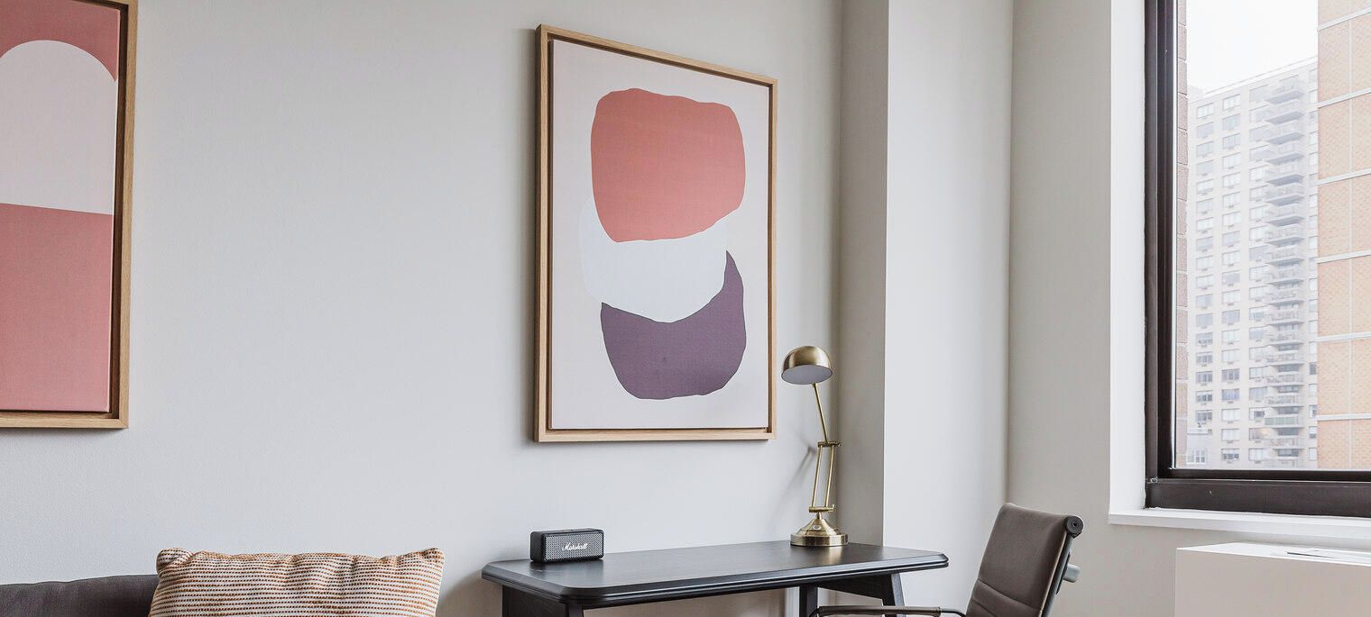A room with a desk, a lamp, and a framed abstract painting on the wall.