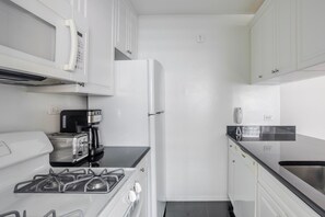 A compact kitchen with white cabinets, a gas stove, a coffee maker, and a refrigerator. - Blueground | Kips Bay, pool, nr Madison Square Park (New York)