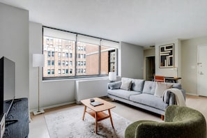 A modern living room with a sofa, a coffee table, a TV, and a large window with a view of buildings. - Blueground | Kips Bay, pool, nr Madison Square Park (New York)