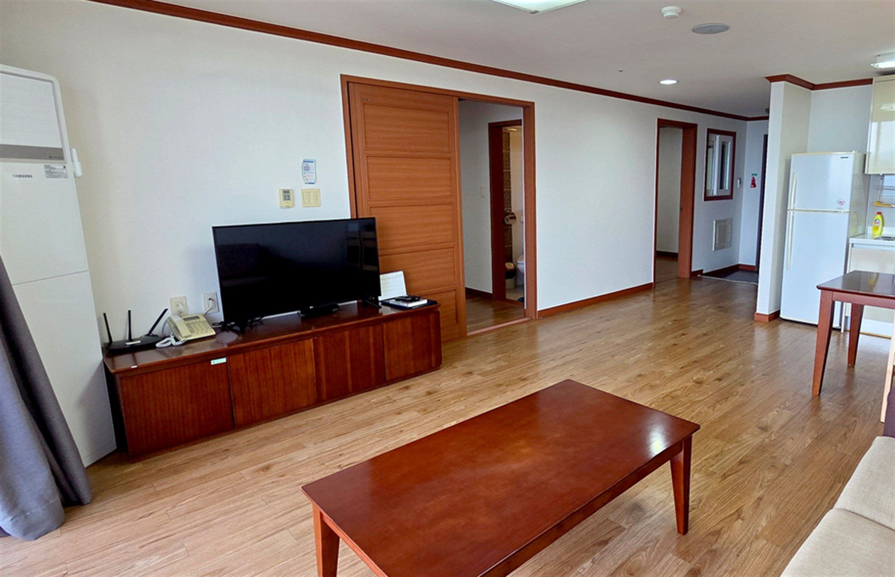 A spacious living area with a wooden entertainment unit, a flat-screen TV, and a dining table.