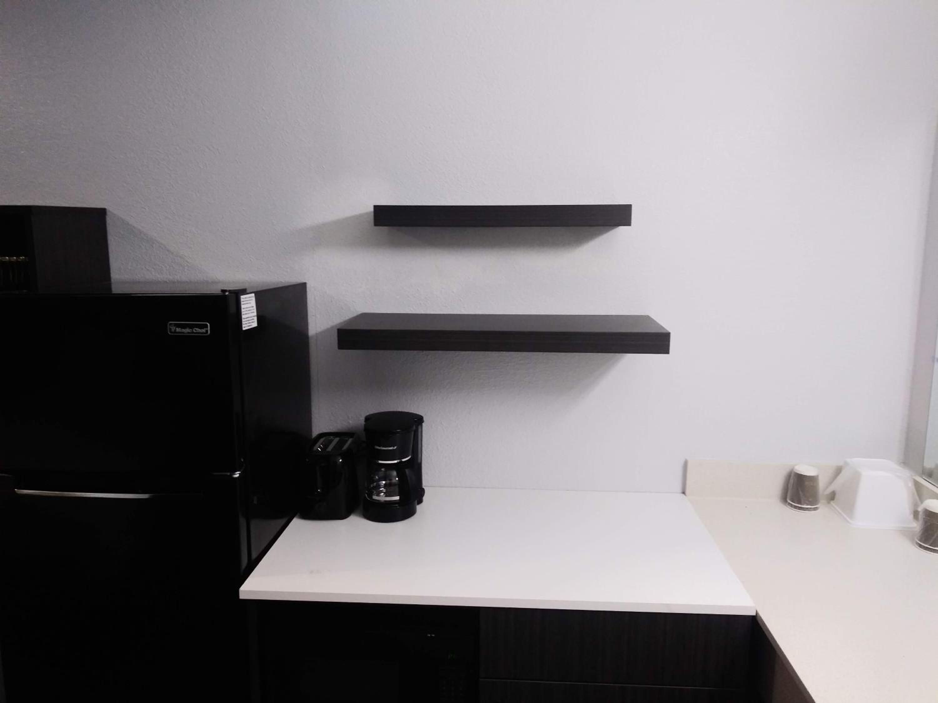 A kitchen with a black refrigerator, a coffee maker, and two black shelves on the wall.