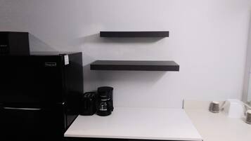 A kitchen with a black refrigerator, a coffee maker, and two black shelves on the wall.