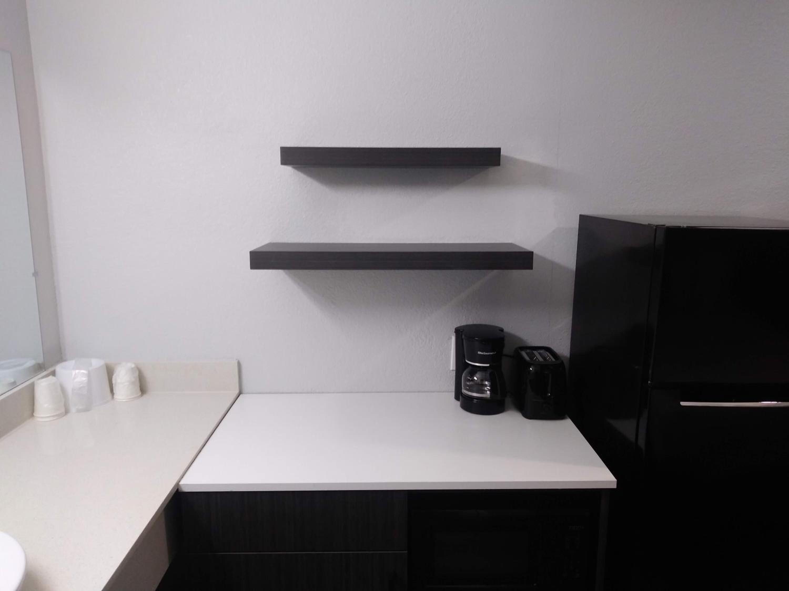 A kitchen with a white countertop, two black shelves, a coffee maker, and a toaster.
