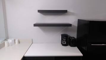 A kitchen with a white countertop, two black shelves, a coffee maker, and a toaster.