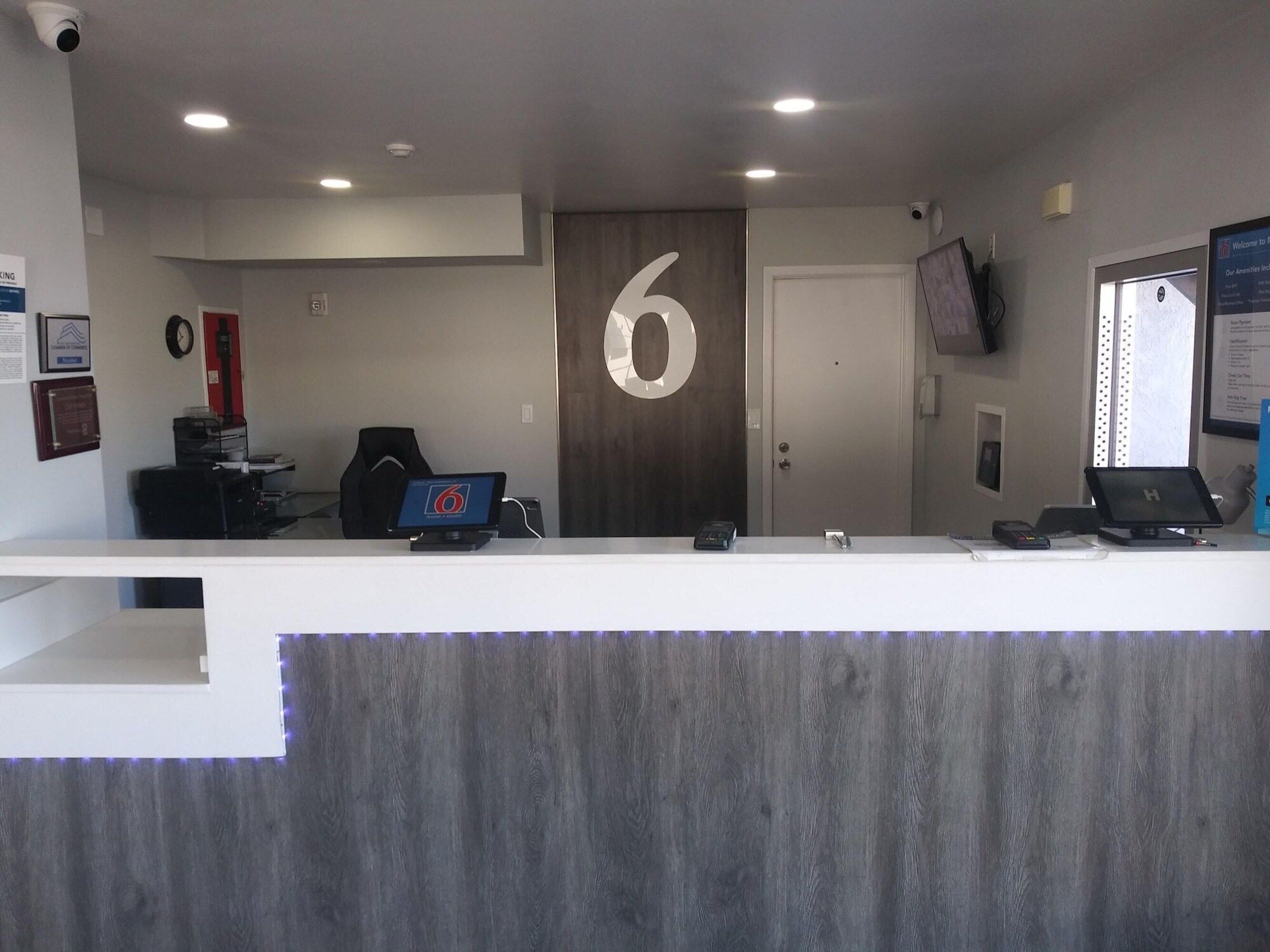 A reception desk with a large number '6' on the wall, a clock, and a mounted television.