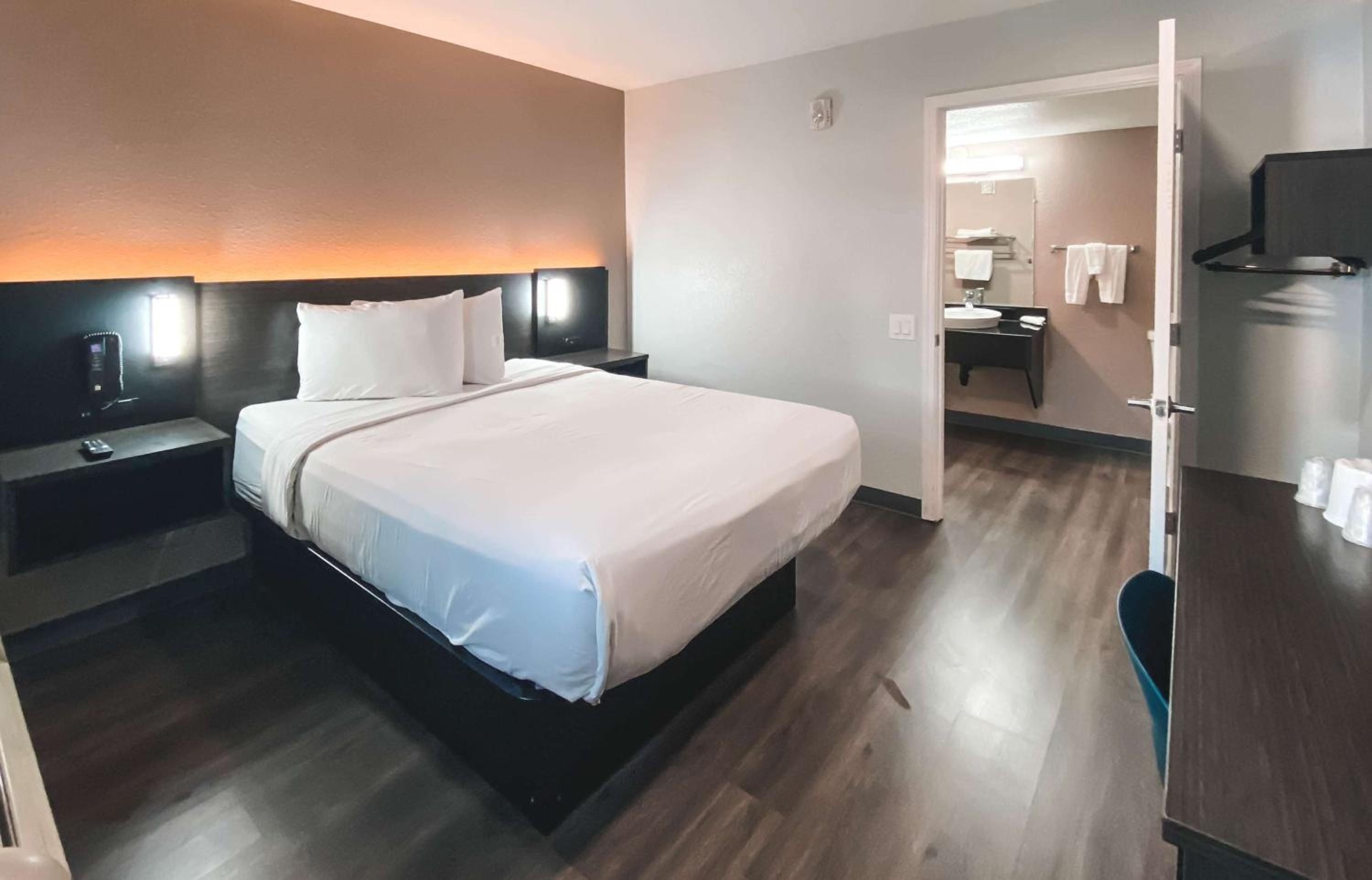 A hotel room with a bed, bedside table, nightstand, and a bathroom visible through an open door.