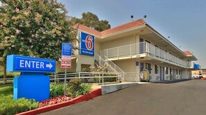 A motel with a sign indicating an entrance, a staircase leading to the building, and a parking lot. - Budget & Pet-Friendly Room | California State Railroad Museum - 2.6 Miles Away (West Sacramento)