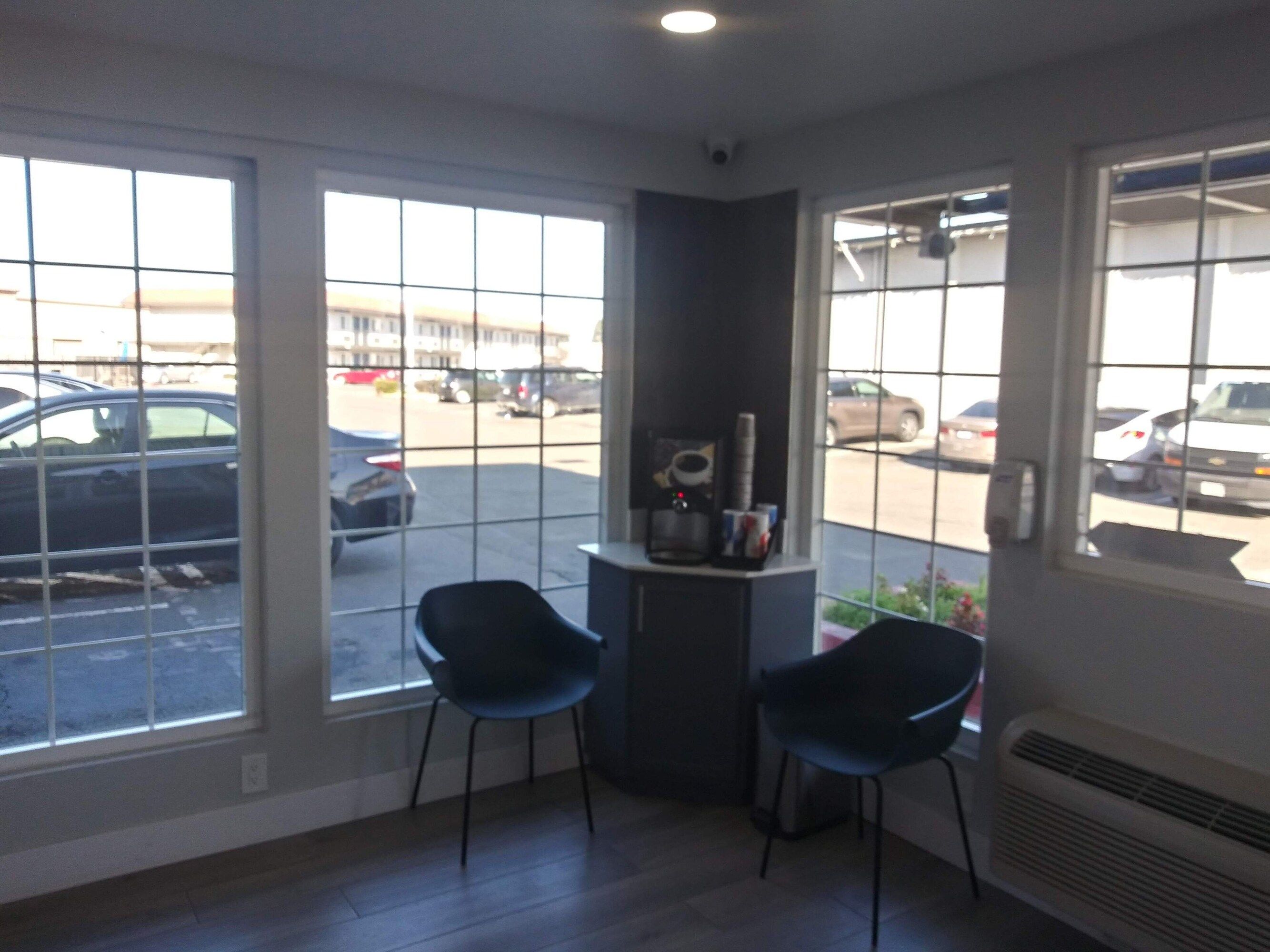 A room with large windows, two chairs, a small table with a coffee machine, and a radiator.