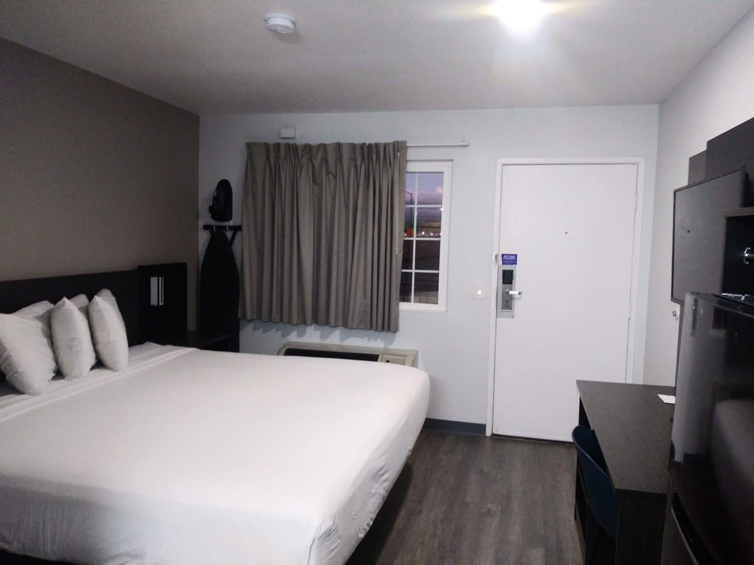 A hotel room with a bed, a desk, a television, a door, and a window with curtains.