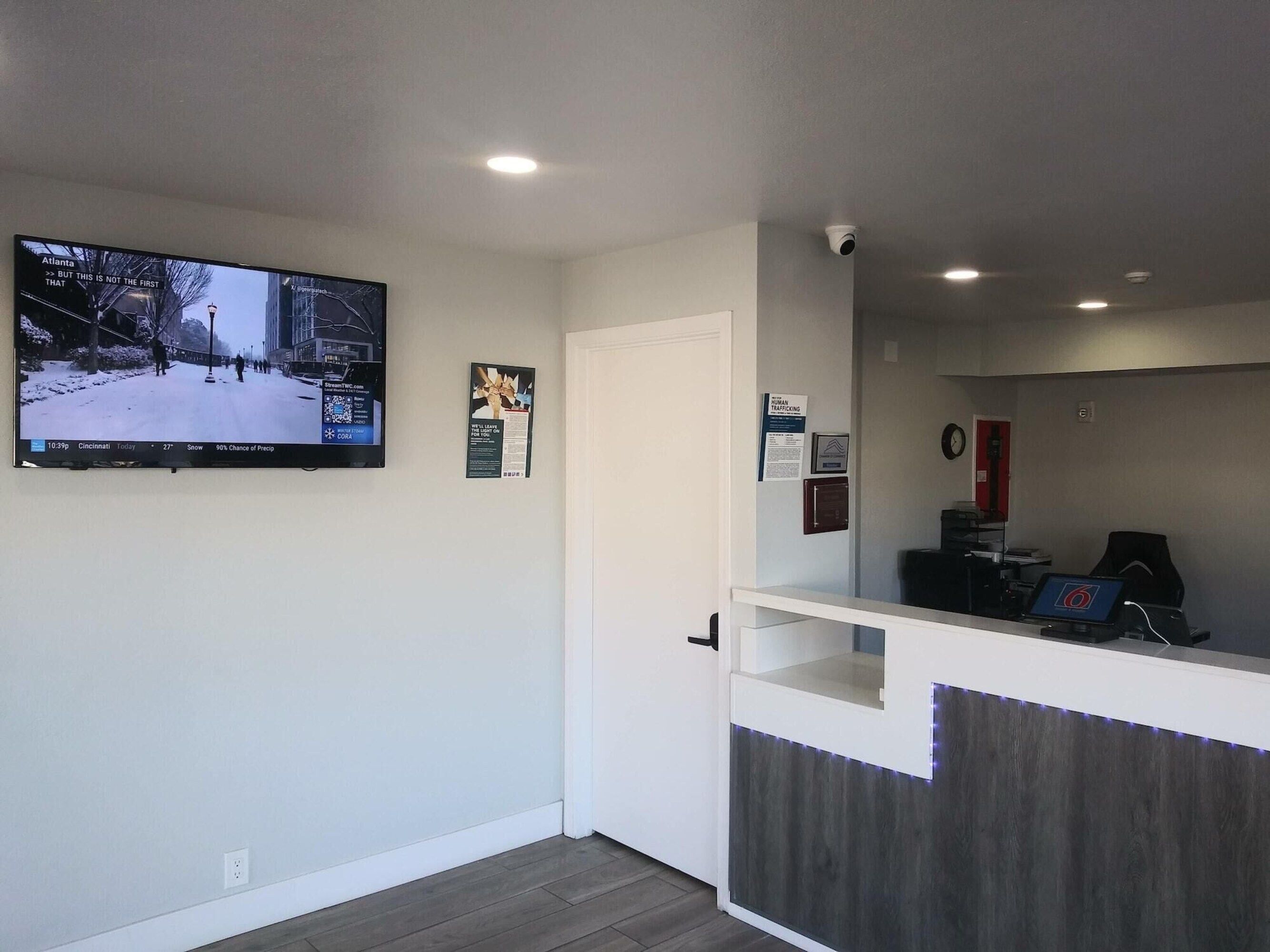 A reception area with a flat-screen TV displaying a snowy street scene, a door, a counter with a computer, and a security camera.
