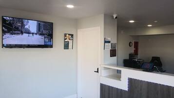 A reception area with a flat-screen TV displaying a snowy street scene, a door, a counter with a computer, and a security camera.