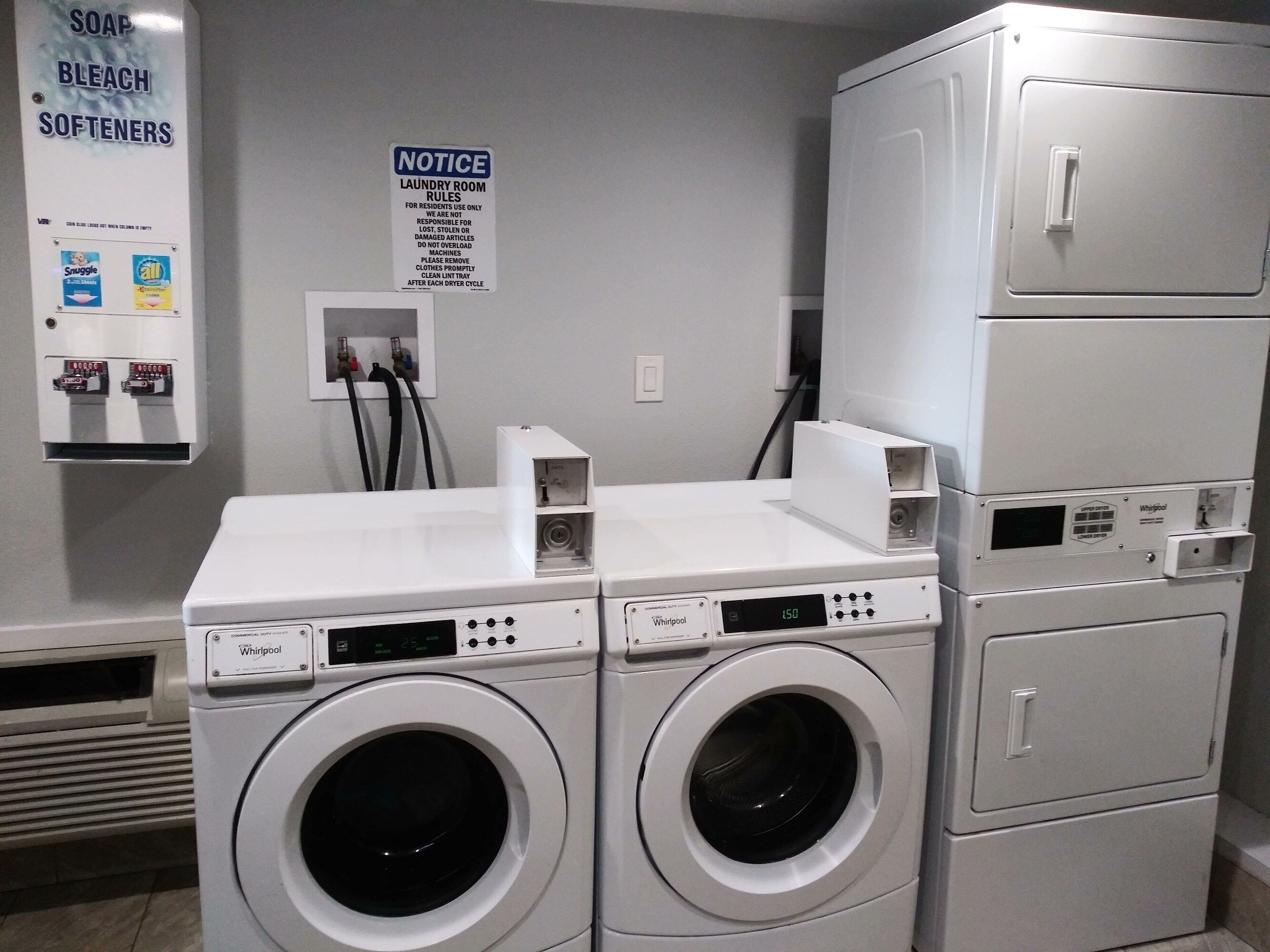 A laundry room with two Whirlpool washers, a notice board, and a utility box.