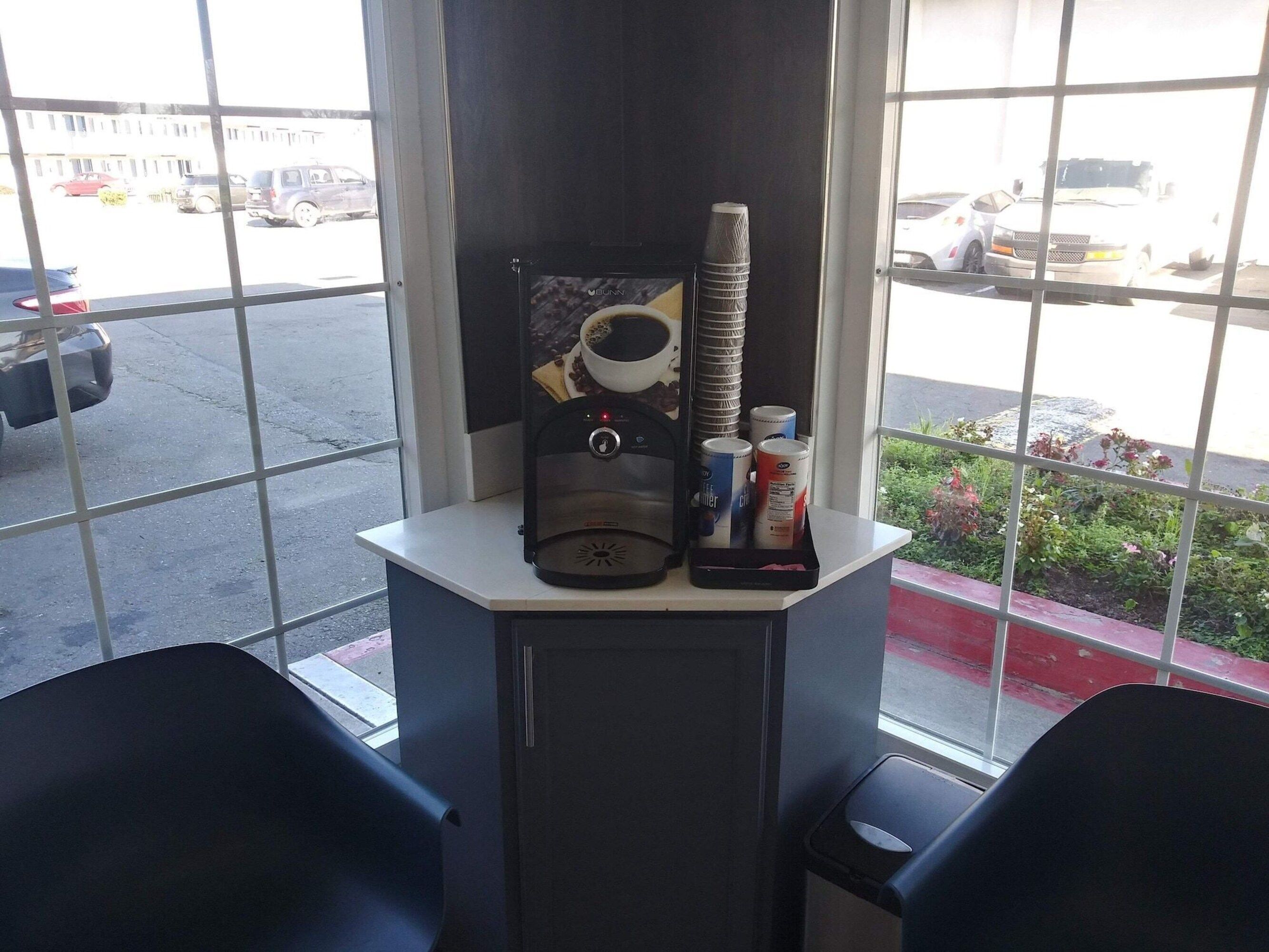A window with a coffee machine, stacked cups, and a trash bin.
