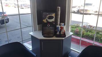 A window with a coffee machine, stacked cups, and a trash bin.