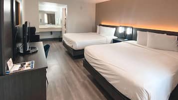 A hotel room with two beds, a desk with a computer, a mirror, and a bathroom visible through an open door.