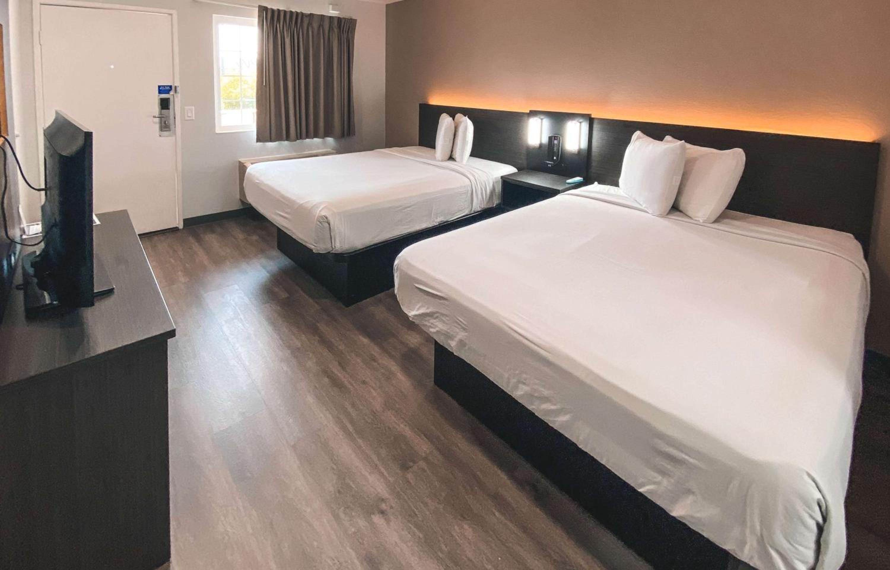A hotel room with two beds, a desk, a TV, and a window with curtains.
