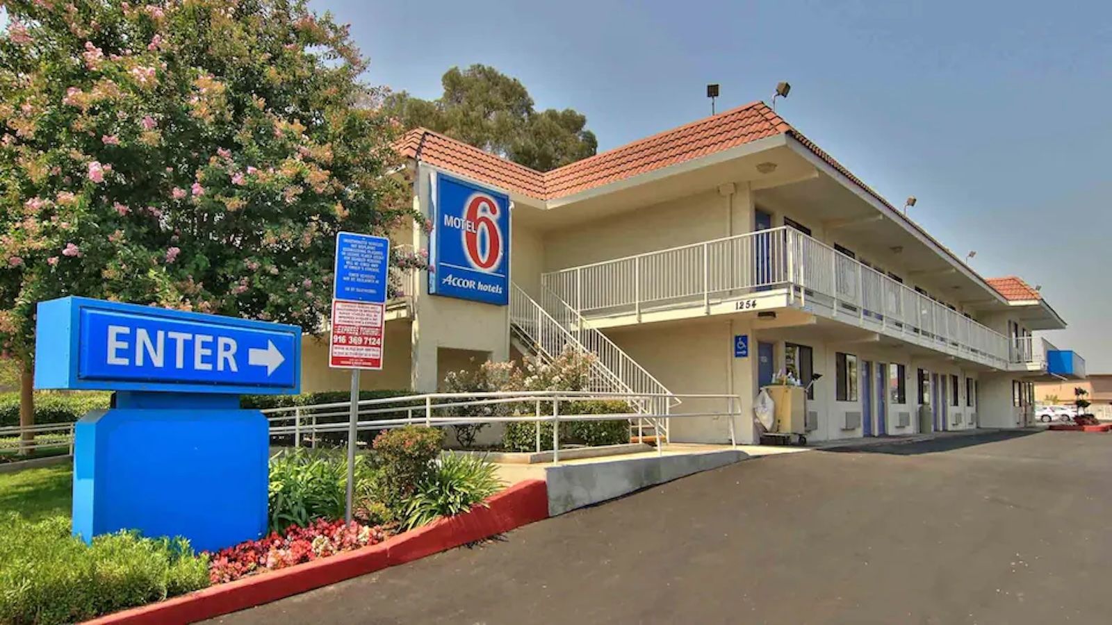 A motel with a sign indicating an entrance, a staircase leading to the building, and a parking lot.
