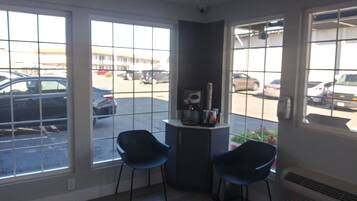 A room with large windows, two chairs, a small table with a coffee machine, and a radiator.
