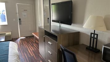 A hotel room with a bed, desk, chair, TV, lamp, and a door.