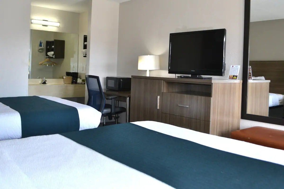 A hotel room with two beds, a desk with a chair, a television, a mirror, and a cabinet.