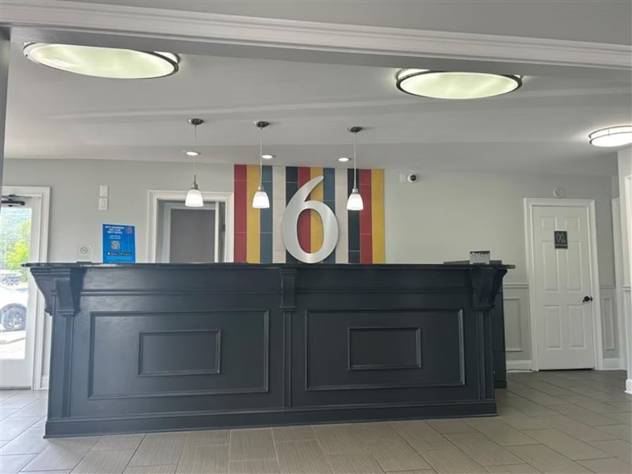 Un espace d’accueil doté d’un comptoir noir, de trois suspensions et d’un motif vertical coloré sur le mur.