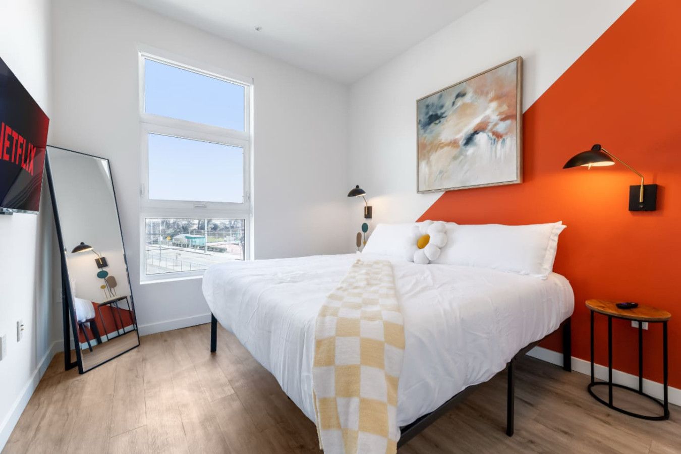 Une chambre d’hôtel avec un grand lit, une fenêtre, un tableau, une lampe et une petite table.