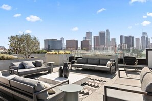 Una terraza en la azotea con mobiliario moderno para exteriores, vista al horizonte de la ciudad y un cielo azul despejado.