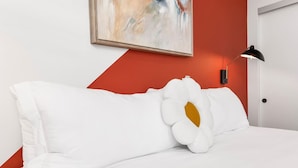 A bed with white bedding and a large white pillow with a yellow center, a black desk lamp, and a painting on the wall. - The DTLA Haven, 1Mi to Dodger Stadium, Free Parking (Los Angeles)