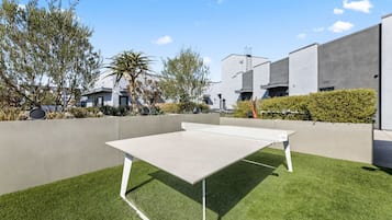 Una mesa de ping pong sobre césped artificial con un edificio moderno al fondo.