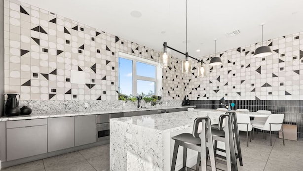 A modern kitchen with a geometric tile backsplash, a large island with bar stools, and a dining area with a white table and chairs. - The DTLA Haven, 1Mi to Dodger Stadium, Free Parking (Los Angeles)