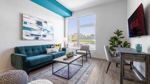 A modern living room with a blue sofa, a coffee table, and a TV mounted on the wall. - The DTLA Haven, 1Mi to Dodger Stadium, Free Parking (Los Angeles)