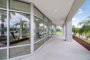 A covered corridor with large windows, a concrete floor, and a view of palm trees and greenery outside. - 2 Rooms w/ Kitchen, Free Parking + Pool Access (Ingleside)