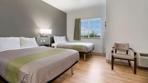 Een hotelkamer met twee bedden, een stoel, een raam met gordijnen en een wandlamp.