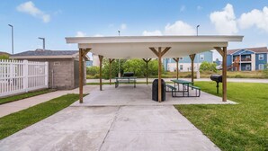 Een overdekte picknickplaats met tafels, banken, een vuilnisbak en een barbecue.