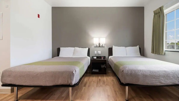 Een hotelkamer met twee bedden, een nachtkastje, een lamp en een raam met gordijnen.
