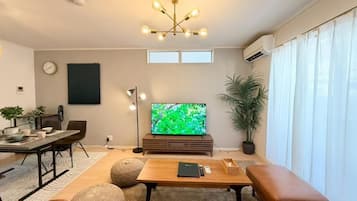 A modern living room with a flat-screen TV, a coffee table, a sofa, and a dining area with a table and chairs.