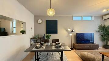A modern living room with a dining area, a flat-screen TV, and a large window.