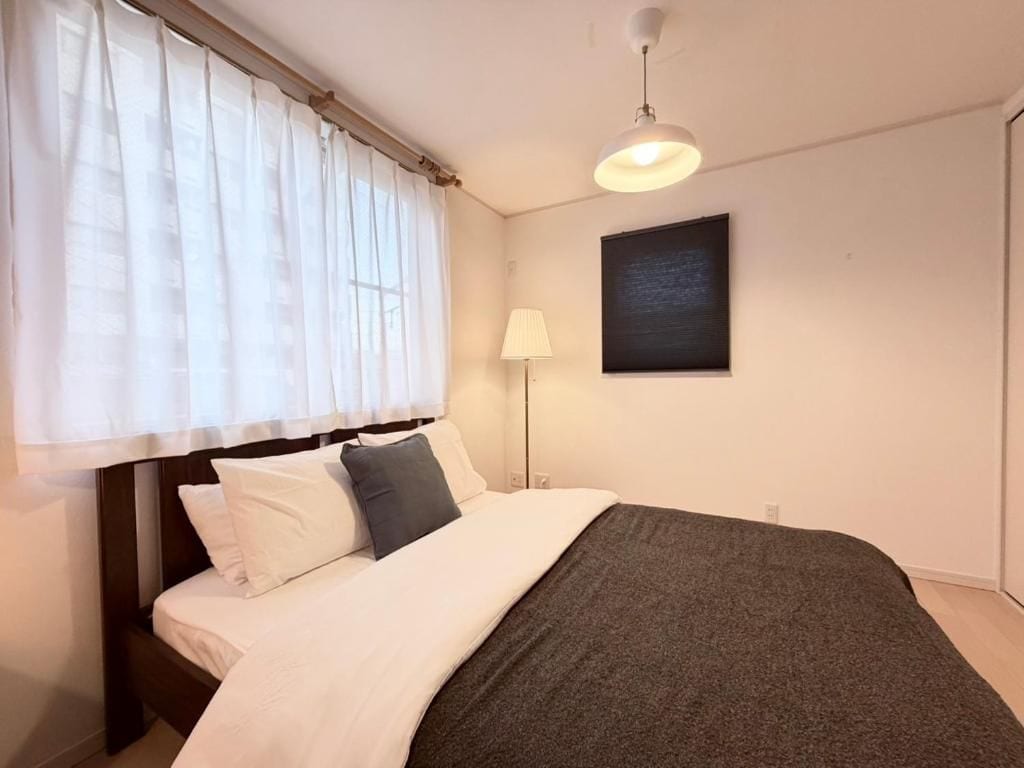 Een slaapkamer met een bed, een bedlamp, een raam met gordijnen en een kunstwerk aan de muur.