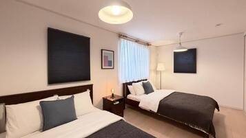 A hotel room with two beds, a nightstand with a lamp, a ceiling light, and a window with curtains.