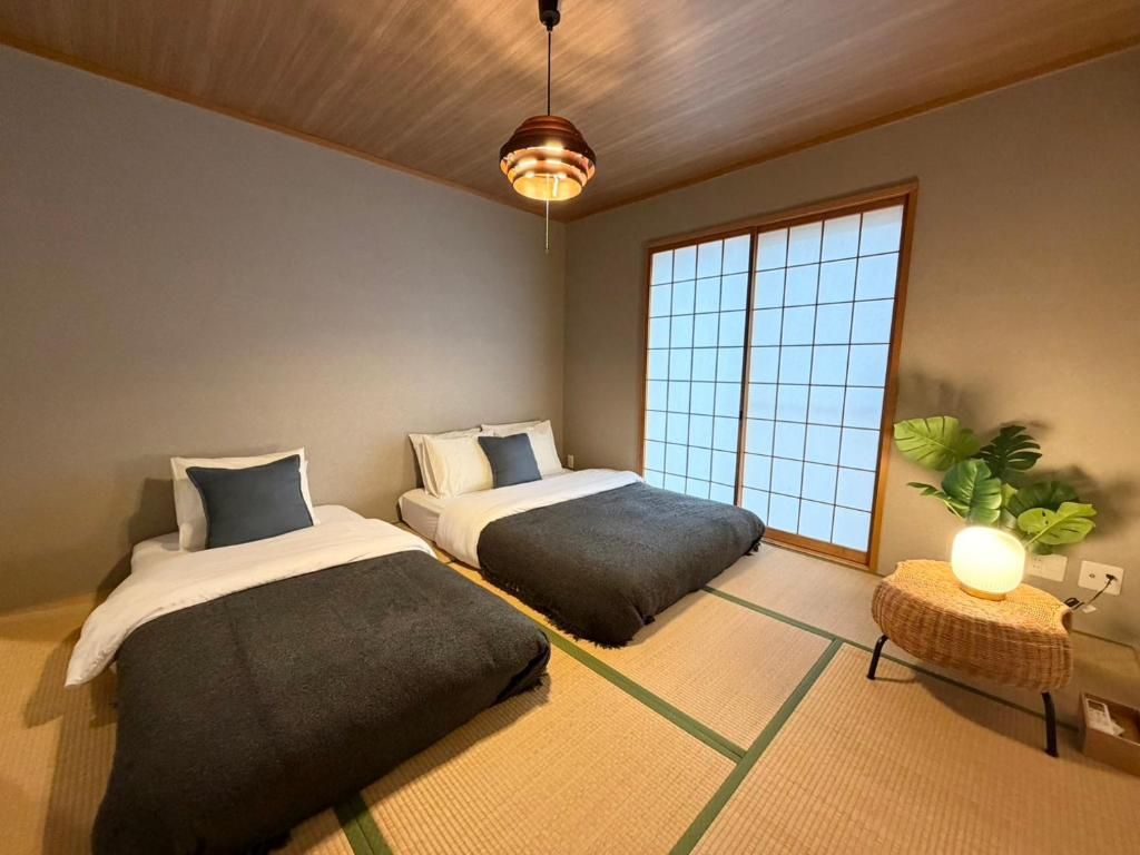 Une chambre avec deux lits, une grande fenêtre et une lampe de style japonais traditionnel.