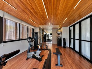 Ein Fitnessraum mit Trainingsgeräten, Holzboden und großen Fenstern.