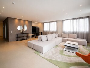 Ein modernes Wohnzimmer mit einer Eckcouch, einem Essbereich mit Tisch und Stühlen sowie einer Küche im Hintergrund.