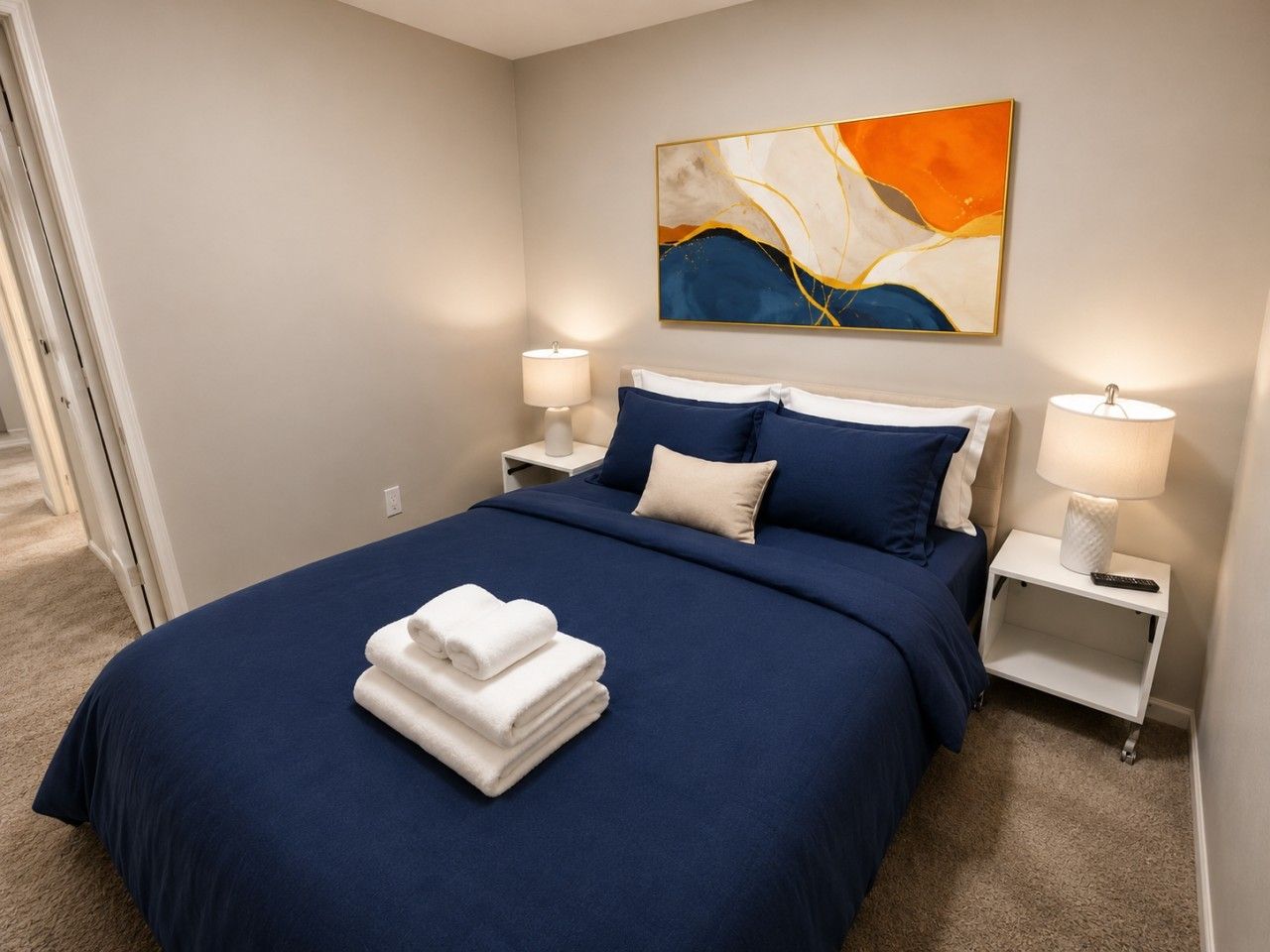 A hotel room with a bed, two bedside tables, a painting, and a pair of towels.