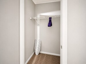 A corner of a room with a white door, a white wall, a brown carpet, a white wall-mounted shelf, and a white wall-mounted ironing board.