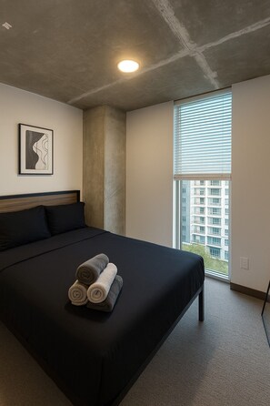 Een hotelkamer met een groot bed, een raam met zonwering, een plafondlamp en een lijst met een afbeelding aan de muur.