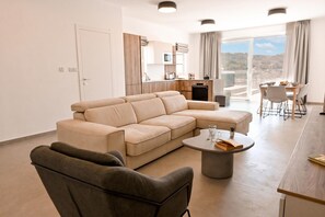 A modern living room with a sectional sofa, a round coffee table, and a dining area with a table and chairs. - Penthouse, Jacuzzi & Sea-view In Gozo 7b, Marsalforn Iz-Zebbug Gozo, Malta (Marsalforn Iz-Zebbug Gozo)