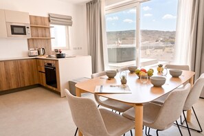 Eine moderne Küche mit Mikrowelle, Toaster und Wasserkocher, einem Esstisch mit Stühlen sowie Blick auf eine Stadtlandschaft durch große Fenster.